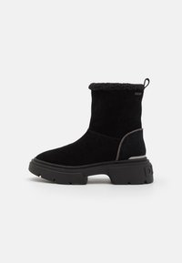 Bottines noires en daim avec une doublure en fauve douce. Semelles en caoutchouc chunky et design minimaliste. Branding subtil sur le côté extérieur.