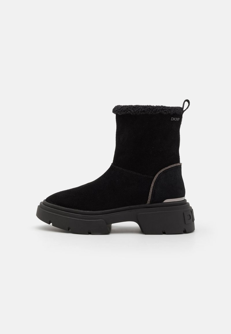 Bottines noires en daim avec une doublure en fauve douce. Semelles en caoutchouc chunky et design minimaliste. Branding subtil sur le côté extérieur.