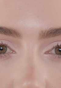 Close-up van menselijke ogen met bruine iris en lange wimpers, met goed verzorgde wenkbrauwbogen en een gladde, lichte huidtextuur.