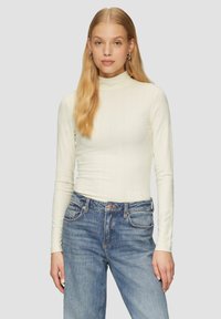 Langärmliges, cremefarbenes, geripptes Rollkragenoberteil, kombiniert mit hellblauen Denim-Jeans im klassischen Fünf-Taschen-Design und mit Knopfverschluss.