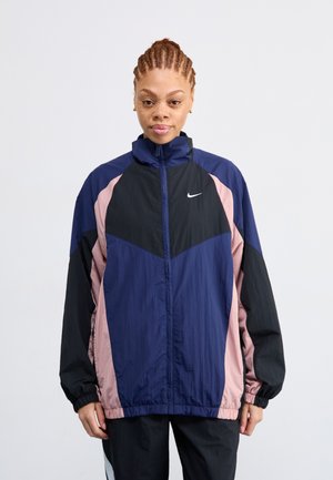 Nike Windbreaker-Jacke mit einem Reißverschluss vorne, hohem Kragen, Navy- und Schwarzen Farbkombinationen mit pinken Akzenten und elastischen Bündchen.