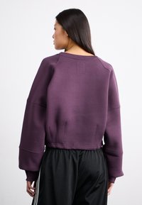 Lilla avkortet genser med brede ermer og ribbede mansjetter. Har et enkelt design med subtile sømdetaljer. Brukt med svarte bukser.