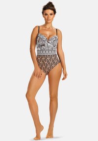 Czarny i biały jednoczęściowy strój kąpielowy z wzorem liści na górze i geometrycznym wzorem w brzoskwiniowym kolorze na dole. Regulowane ramiączka.