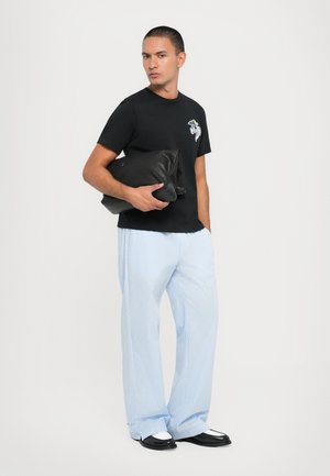 Black t-shirt with graphic design, light blue striped wide-leg pants, and black clutch bag. Two-tone shoes with a white accent detail.
