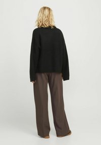 Suéter negro de punto con corte holgado, textura acanalada y mangas anchas, combinado con pantalones marrones de pierna ancha. Fondo neutro.