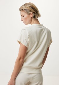 Cremfarbener Kurzarm-Top mit rundem Halsausschnitt, leichtem Stoff, taillierter Saum und weicher Textur. Glatte Verarbeitung, geeignet für die Freizeit.