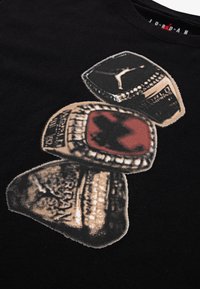 Tricou negru cu un grafic ce reprezintă trei inele de campionat cu gravuri detaliate și accente roșii, imprimate într-un stil șters.