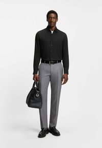 Camicia nera a maniche lunghe con bottoni, pantaloni grigi su misura, cintura e scarpe nere. Tiene una borsa in pelle nera. Tessuto liscio e design elegante.