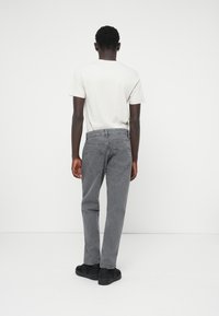 Jeans in denim grigio con una vestibilità rilassata, quattro tasche e una cintura elastica. Abbinati a una maglietta chiara e a sneakers nere.