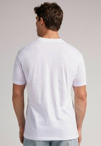 Bílý bavlněný tričko s krátkým rukávem, kulatým výstřihem, hladkou texturou a rovním lemem. Žádné vzory ani další detaily nejsou viditelné.