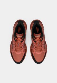 Bežecké topánky Saucony v koralovej a čiernej farbe, s textúrovaným sieťovaným zvrškom, polstrovaným golierom a hrubou čiernou gumovou podrážkou.