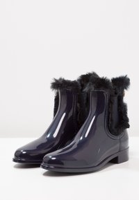 Navy waterproof ankle boots with shiny finish, faux fur trim at the top, flat heel, and elastic side panels for easy slip-on wear.