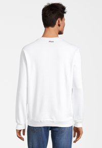 Felpa bianca con maniche lunghe, polsini e orlo a costine, con un piccolo logo FILA rosso e blu sul retro del collo. Materiale in cotone testurizzato.