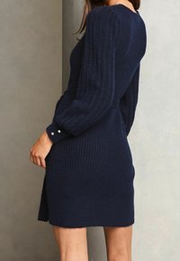 Mörkblå ribbad klänning i sweatshirtmaterial med långa ärmar, knapparseende vid ärmsluten och en figurnära silhuett med en liten sidslits.