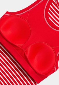Reggiseno sportivo rosso con coppe sagomate, scollatura rotonda e un bordo a strisce rosso e bianco nella parte inferiore. Tessuto liscio con cuciture a contrasto.