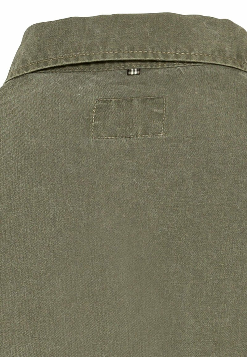 Olijfgroene blouse met een kraag, voorzien van een rechthoekige patch en zichtbare stiksel. De stof lijkt zacht en gestructureerd te zijn.