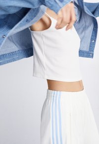 White ribbed crop top paired with light blue striped drawstring pants, complemented by a denim jacket with buttoned front and cuff details.