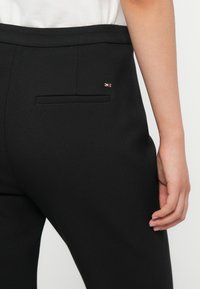 Pantaloni neri su misura con una texture liscia, con tasca posteriore e piccolo logo colorato accentato vicino alla vita.