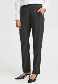 Zwarte gestreepte broek van geweven stof, met een gladde textuur en zijzakken. Gecombineerd met zwarte puntige hakken.