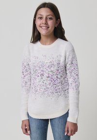 Weißer Pullover mit strukturiertem Finish, ausgestattet mit einem gradienten lila Muster auf der Brust. Rundhalsausschnitt und gerippte Bündchen, kombiniert mit blauen Jeans.