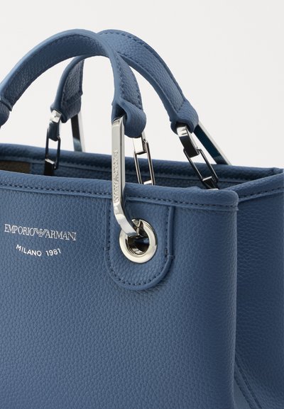 Borsa a mano in pelle blu con finitura texturizzata, dotata di accessori in argento e manici corti. Logo in rilievo sul davanti, dettaglio orecchino metallico circolare.