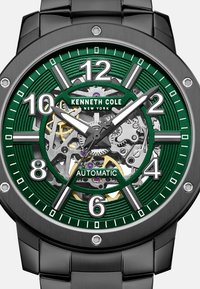 Zwarte roestvrijstalen horloge met een groene geprinte wijzerplaat, zichtbare automatische uurwerk, zilveren uurmarkeringen en bijpassende wijzers.