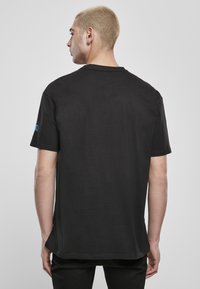 Fekete, rövid ujjú, pamut póló, laza szabással, kerek nyakkivágással és kék logóval a bal ujján. Simás textúra.