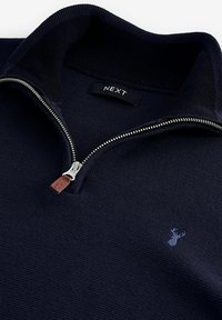 Pulover închise la culoare, de nuanță bleumarin închis, cu guler înalt, fermoar argintiu și etichetă din piele. Dispune de un tricot texturat și un mic logo cu cerb pe piept.