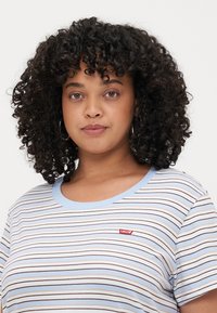 Camiseta a rayas en blanco, azul y marrón con un cuello redondo y parche con el logo de Levi's. Tejido suave con un ajuste relajado y mangas cortas.