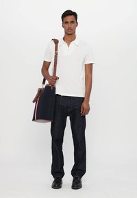 Balta polo marškinėliai su užtrauktuku, tamsiai mėlynos džinsai ir juodi batai. Modelis neša tamsiai mėlyną krepšį su rudomis petnešomis ir raudonu akcentu.