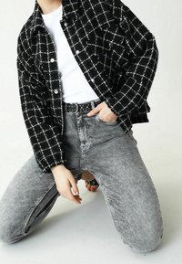 Svart och vit rutig jacka i texturerad tyg, kombinerad med grå denimjeans. Har en figursydd silhuett och ett nitar svart bälte.