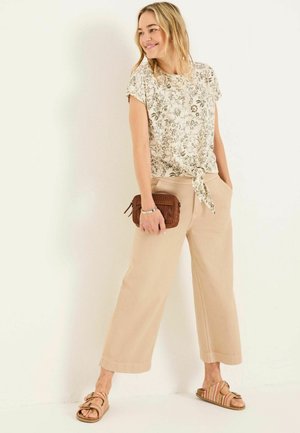 Bluse mit floralem Muster und kurzen Ärmeln, geknotetem Saum, beigen weit geschnittenen Hosen und braunen geflochtenen Sandalen, kombiniert mit einer braunen strukturierten Clutch.