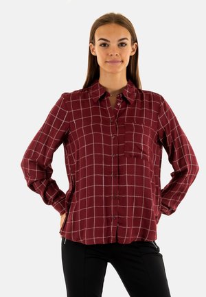 Blouse à carreaux bourgogne avec un devant à boutons, une poche poitrine et des manches longues. Tissu lisse avec des lignes grises et des fentes sur les côtés.