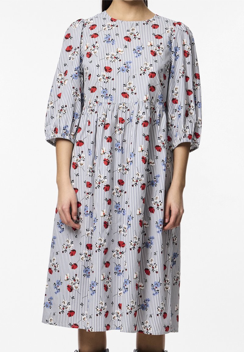 Kukallinen midi-mekko, jossa on sinisiä ja punaisia kukkia valkoisilla ja sinisillä raidoilla. Mekossa on pyöreä pääntie ja puffipuserot, joissa on rypytettyä yksityiskohtaa.