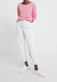Rot-weißt gestreiftes Langarmshirt kombiniert mit hellblauen, hoch taillierten Jeans. Weiße Sneakers vervollständigen das Outfit.