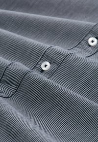 Gestreifter Stoff in Marineblau und Weiß, mit weicher Textur und drei weißen Knöpfen entlang der Knopfleiste. Zerknittertes Aussehen.