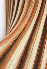 Gros plan sur un tissu plissé avec des rayures verticales aux tons orange, marron, beige et crème, créant un motif texturé.