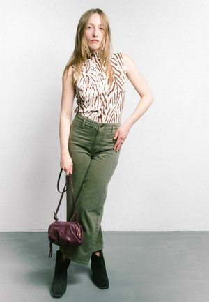 Top senza maniche beige con righe marroni, pantaloni olive green a vita alta, stivali neri alla caviglia e una piccola borsa a tracolla in pelle viola.