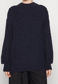 Pull en maille bleu marine avec un motif texturé, doté d'un col rond et de poignets côtelés. Coupe ample, avec un ourlet droit.