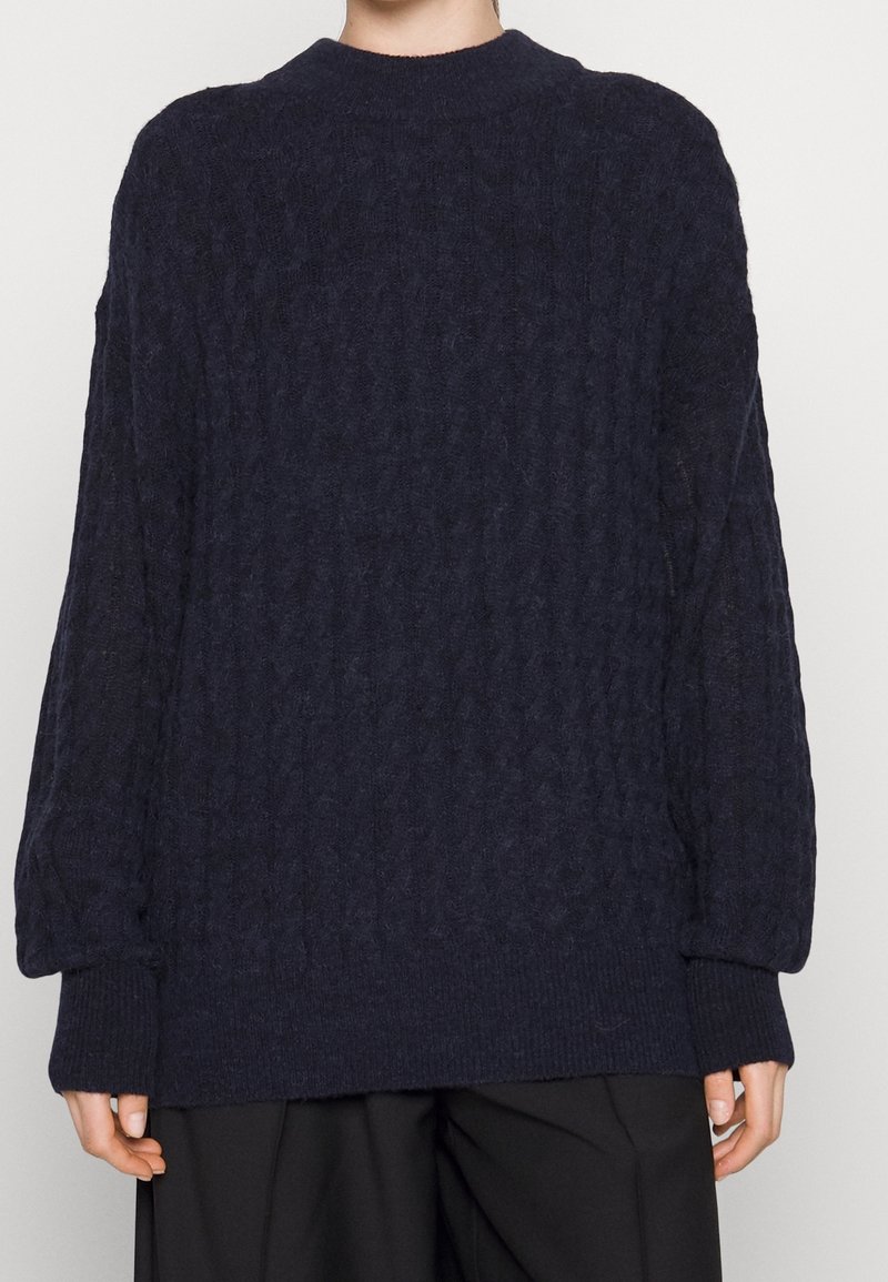 Pull en maille bleu marine avec un motif texturé, doté d'un col rond et de poignets côtelés. Coupe ample, avec un ourlet droit.