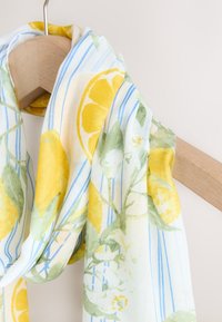 Lekki, półprzezroczysty szalik z żółtymi cytrynami i zielonymi liśćmi na białym tle w niebieskie paski. Miękka tekstura tkaniny.