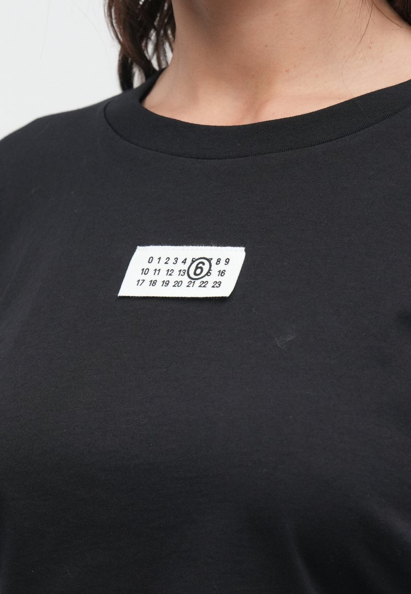 Sort bomulds-T-shirt med rund halsudskæring, med et hvidt stofmærke med tal og et rundt logo foran.