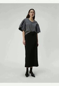 Grå bomullsblandingsgenser med voluminøse ermer, kombinert med en svart, tettsittende maxikjole og spisse svarte hæler. Enkelt, elegant design.