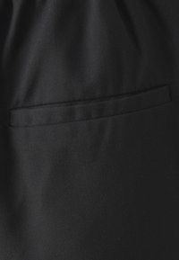 Černá tkanina s hladkým povrchem a diskrétním horizontálním kapsou ve střední výšce. Jednoduchý a minimalistický design.