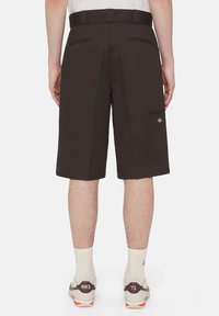Brune shorts med rett snitt, to baklommer og en liten logo på venstre side. Båret med hvite sokker og grå joggesko med oransje detaljer.