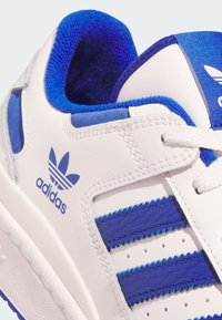 White athletic shoe with blue accents. Features leather material, three blue stripes, and a textured blue interior. Laces and logo prominent.