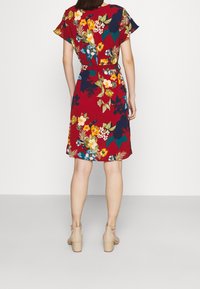 Blommig klänning med röd bas, prydd med flerfärgade blommor, korta ärmar, figurnära midja och knälång längd. Bärs med beige klackar.