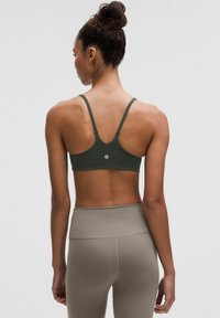 Sujetador deportivo verde oscuro con tirantes finos, diseño de espalda en forma de U y detalle de logo. Combinado con leggings beiges de cintura alta. Textura suave.