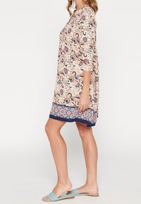 Blumenkleid mit dreiviertel Ärmeln, ausgestattet mit einem beige und mehrfarbigen Design, ergänzt durch einen gemusterten Saum und einem geraden Schnitt.