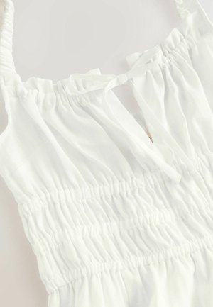 Rochie albă fără mâneci, cu textură plisată și detalii cu fundă la guler, având secțiuni smockate pentru o potrivire elastică.